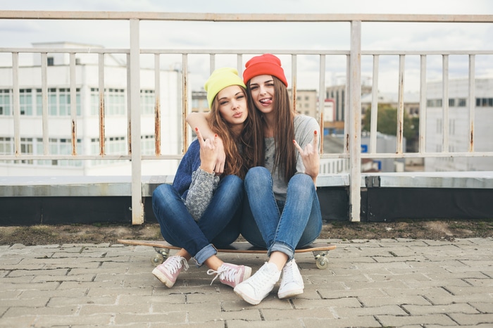 Two young women sitting on a skateboard
