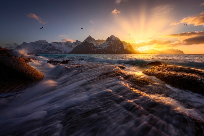 Waves crashing on rocks with mountains and sunset