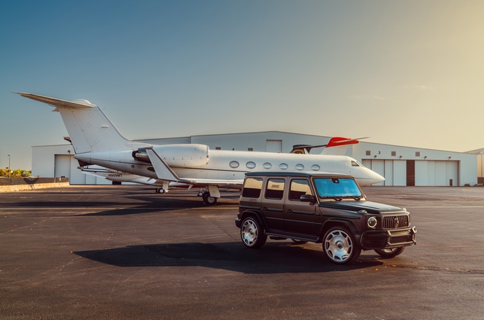 Mercedes G-Class parked by a private jet at an airport hangar