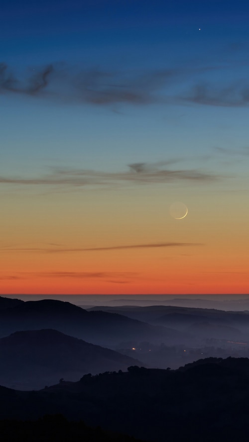 Crescent moon over misty mountains at sunset