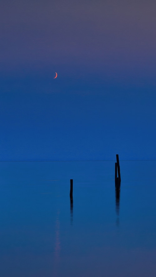 Crescent moon over calm water with posts