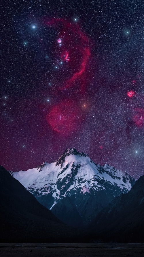 Snow-capped mountains under a starry nebula sky