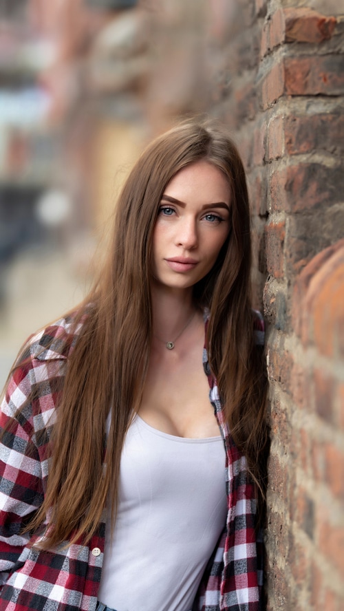 Young woman in plaid shirt leaning against brick wall