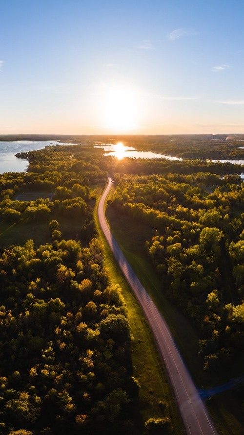 Aerial view of a road through a forest by a lake at sunset