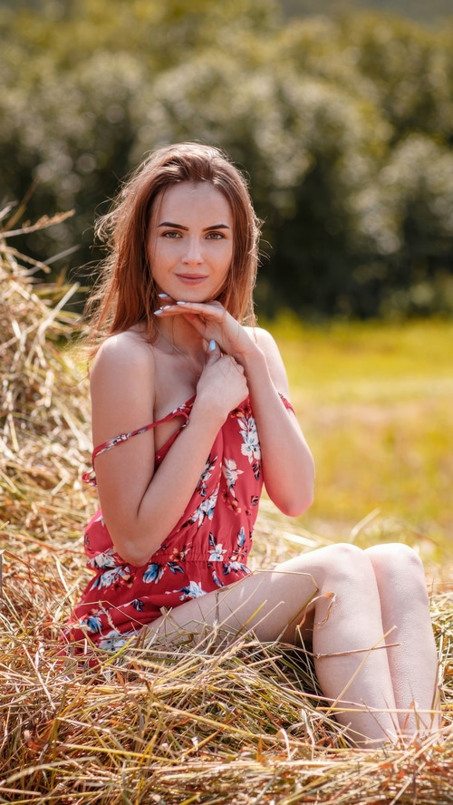 Brunette model in a red dress sitting in hay