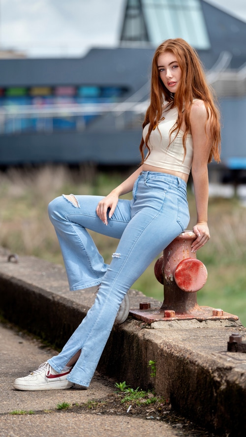 Model in ripped jeans sitting on a bollard