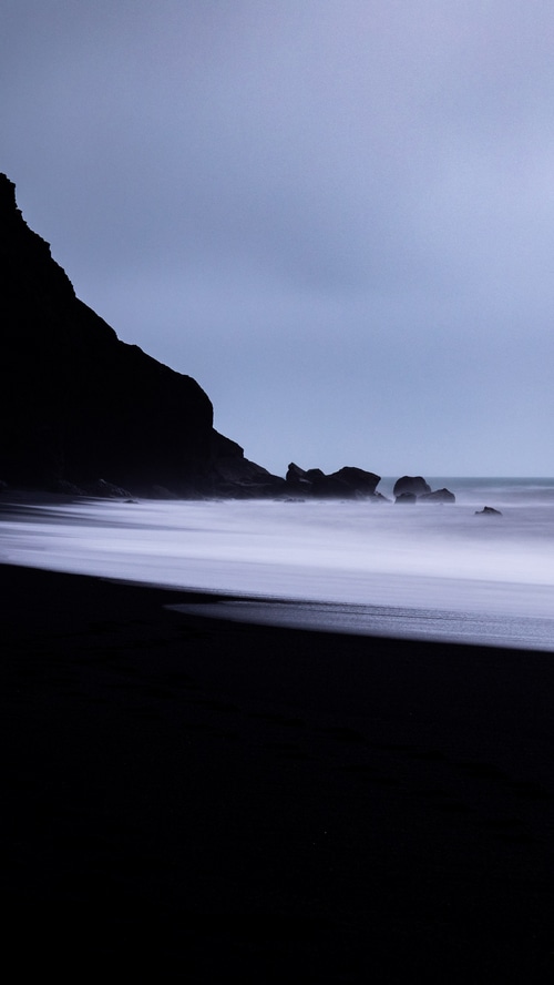 Black sand beach with waves and rock formations