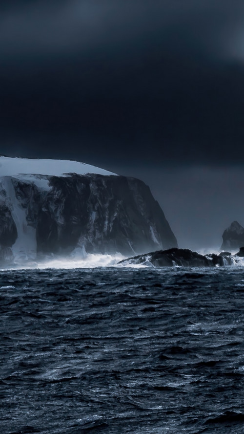 Antarctica coast with stormy seas and snow-capped cliffs