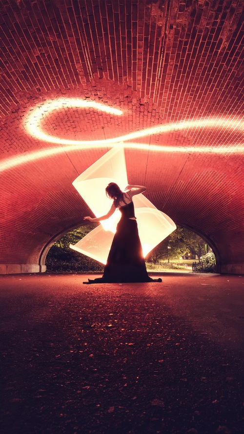 Woman in a black dress with light painting under a brick archway