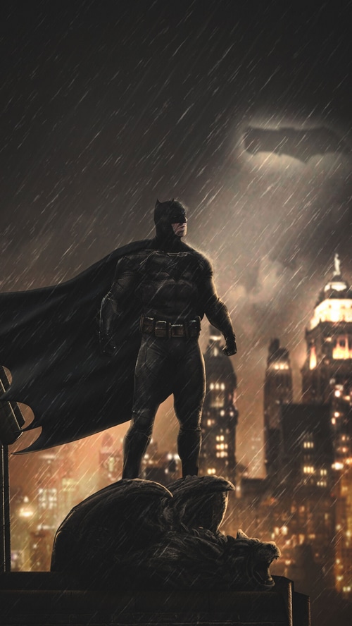Batman standing on a gargoyle in the rain