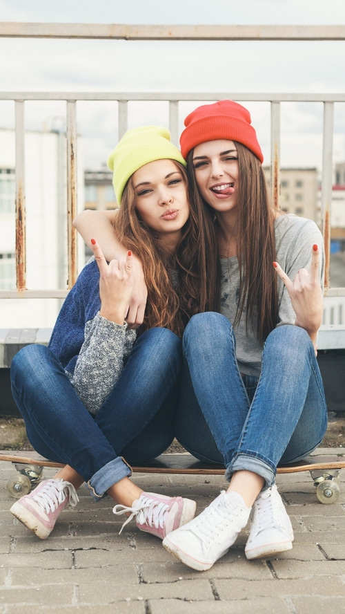 Two young women with beanies on a skateboard