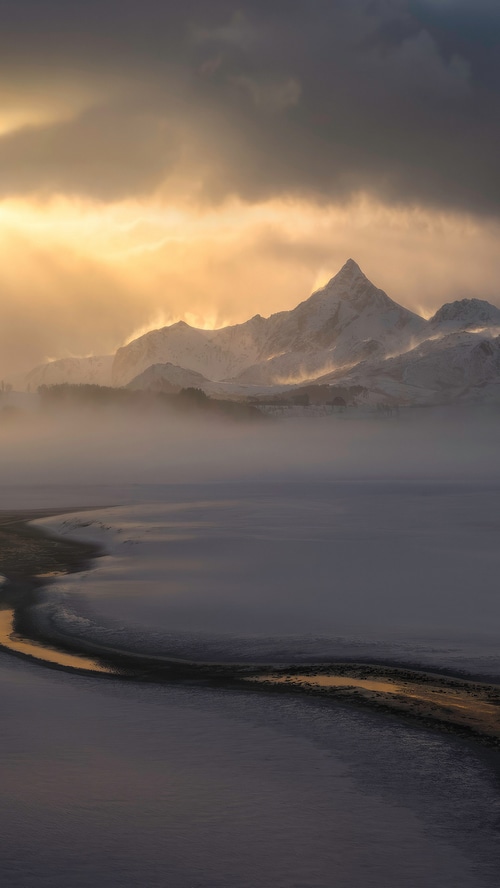 Snowy mountains shrouded in mist during golden hour