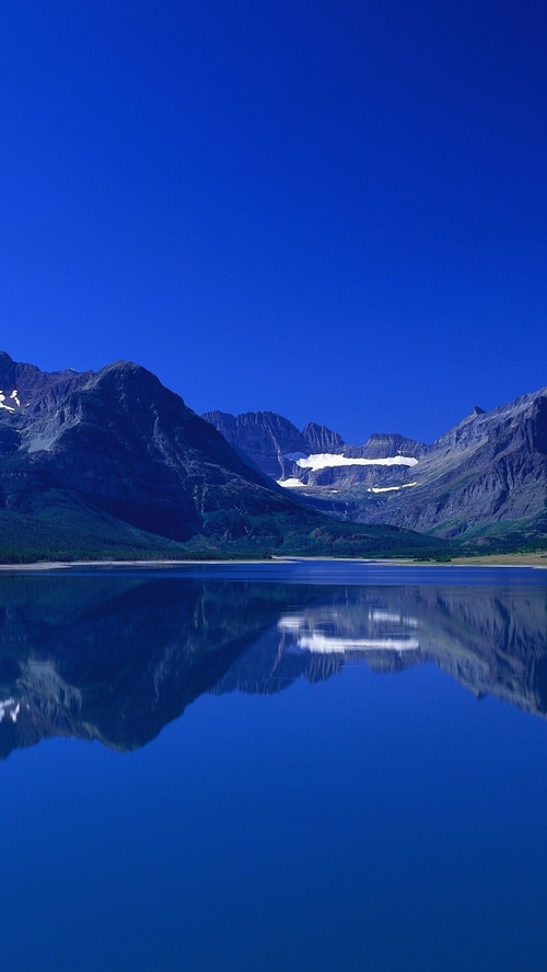 Mountains reflected in a calm lake under a clear blue sky