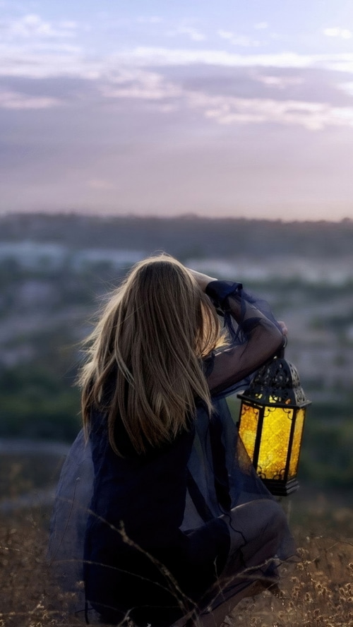 Girl with lantern in field at sunset
