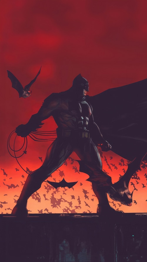 Batman standing with bats against a red sky