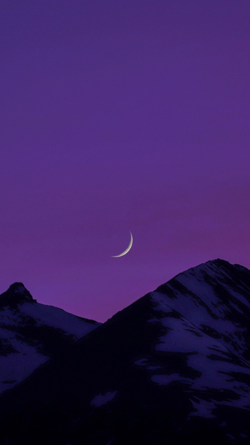 Crescent moon over snow-capped mountains at dusk