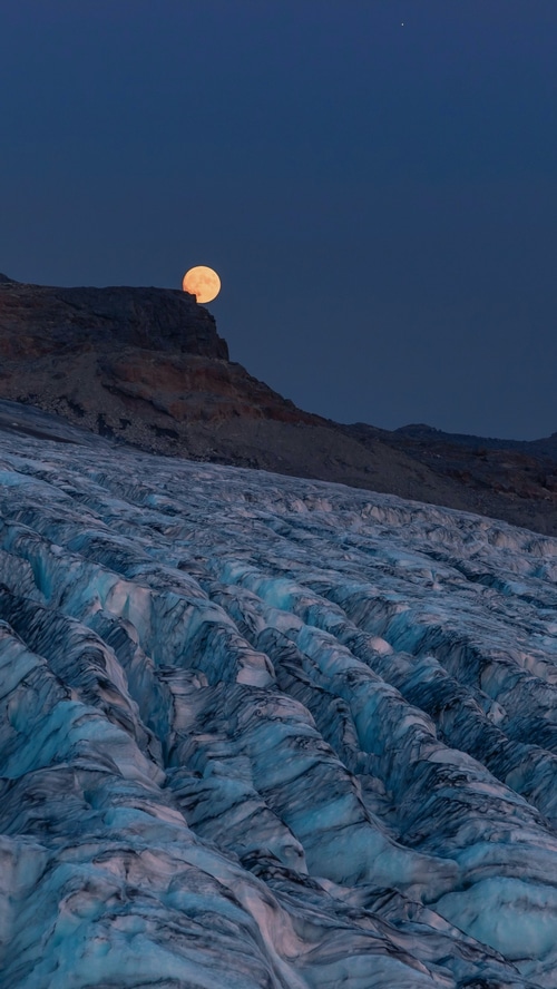 Moon setting over a glacier in the mountains