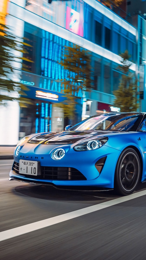 Blue Alpine A110 driving through a city at night