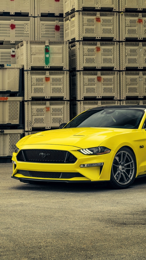 Yellow Ford Mustang parked in front of stacked crates