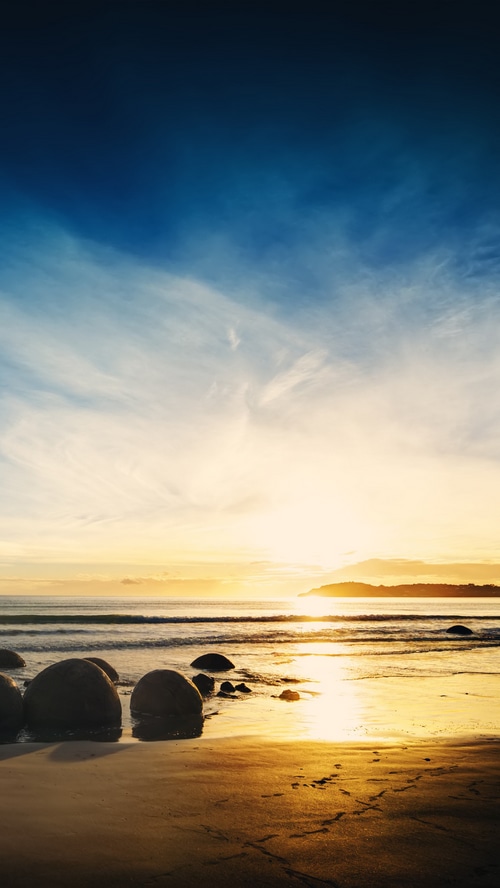 Sunrise over the ocean with large boulders on the beach