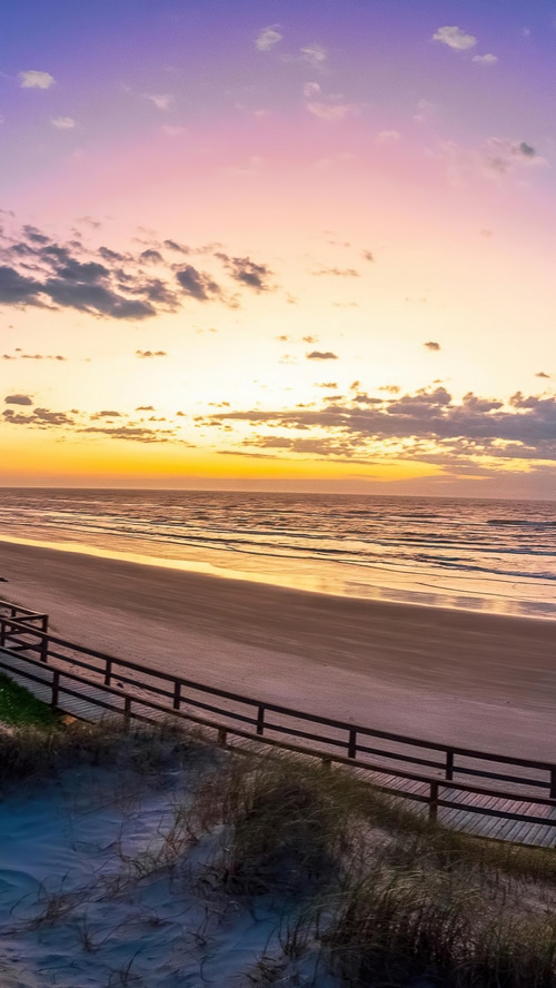 Sunset over a beach with a wooden boardwalk