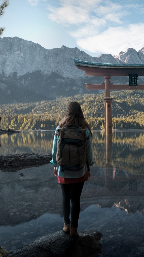 Woman with backpack at a lake with mountains and torii gate