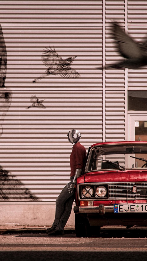 Robot leaning on a red car with birds flying