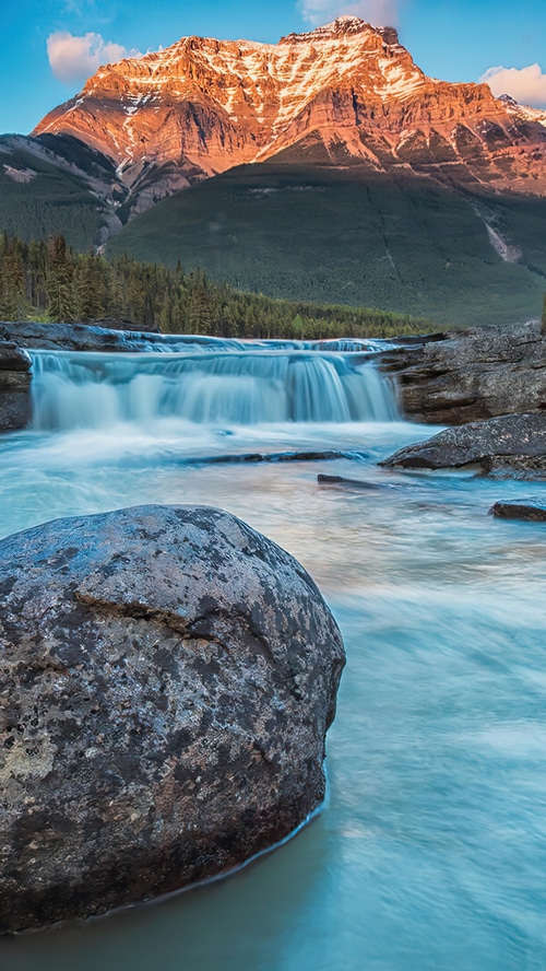 Waterfall cascading down rocks with a mountain in the background