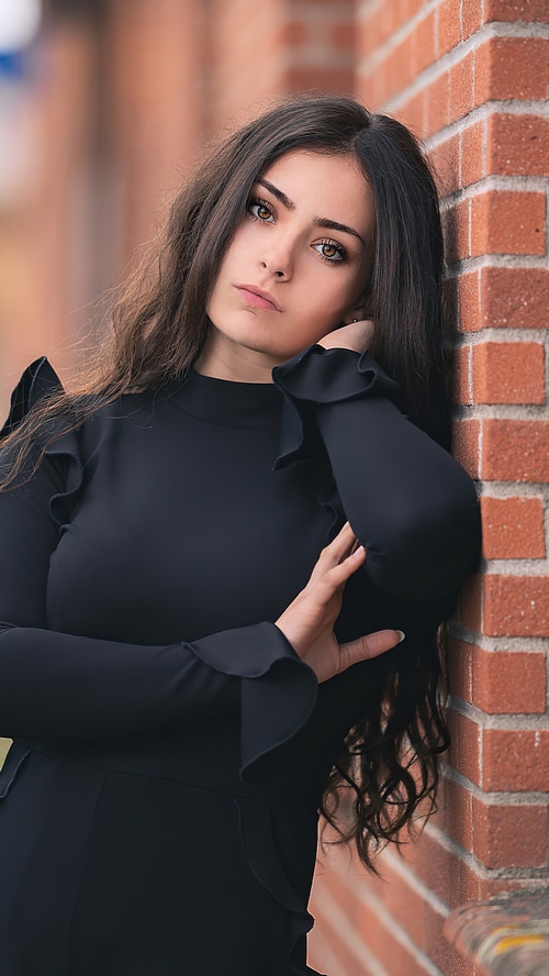 Girl in black dress leaning against brick wall