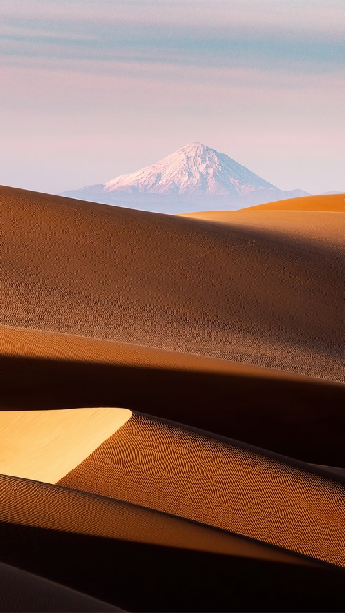 Snow-capped mountain over desert dunes