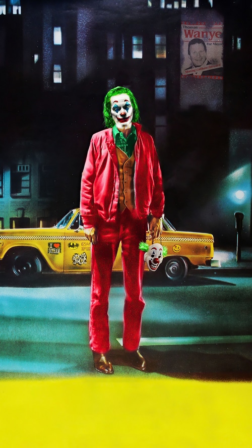 Joker holding a clown mask in front of a taxi