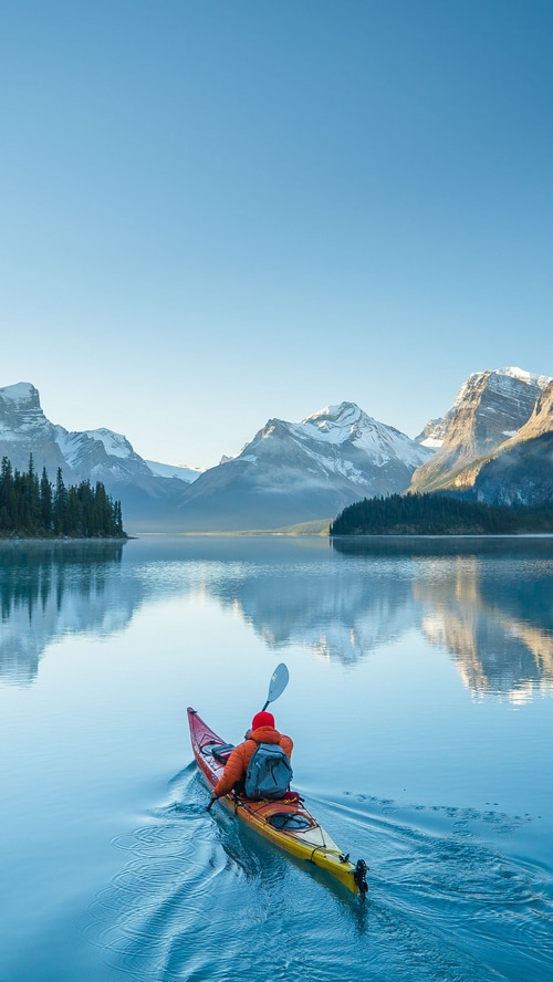 Kayaker on a calm lake with snow-capped mountains