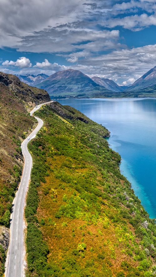 Winding road along a lake with mountains in the background