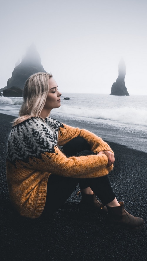 Woman in sweater on black sand beach