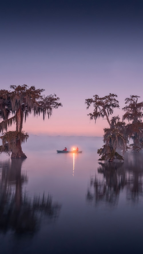 Two people in a boat with lanterns on a misty lake