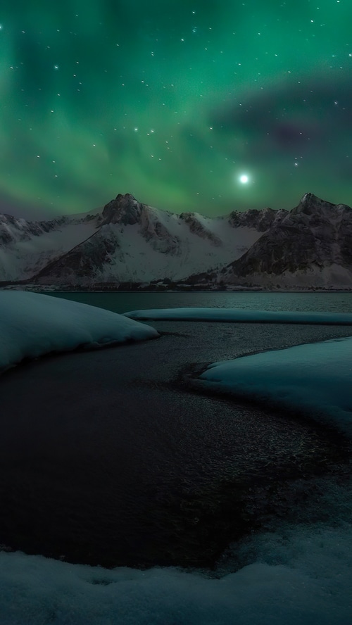 Aurora Borealis over snow-capped mountains and a lake