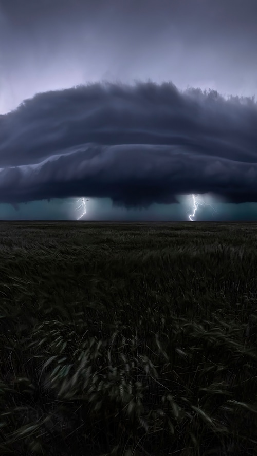Lightning strikes over a dark field under storm clouds