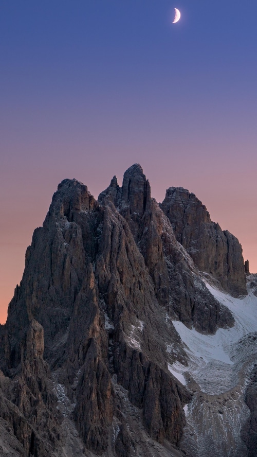 Crescent moon over jagged mountain peaks at sunset