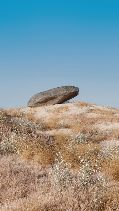 A large rock rests on a grassy hill under a clear blue sky.
