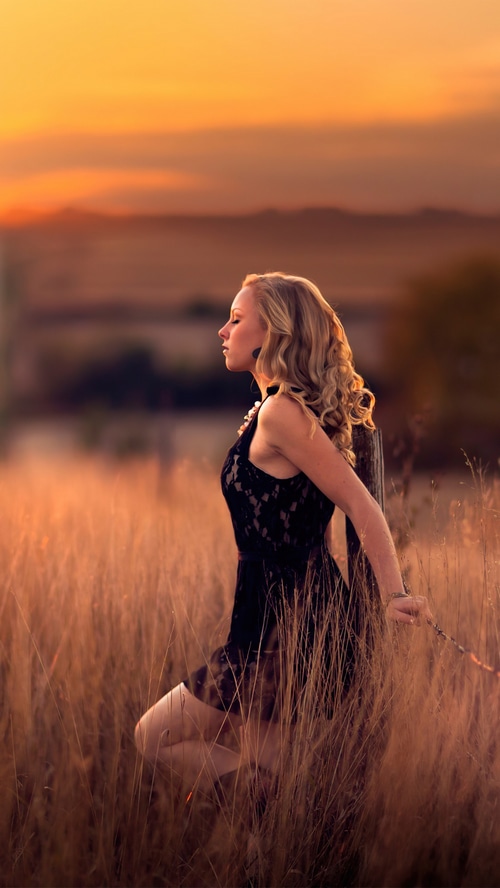 Woman in black dress in a field at sunset