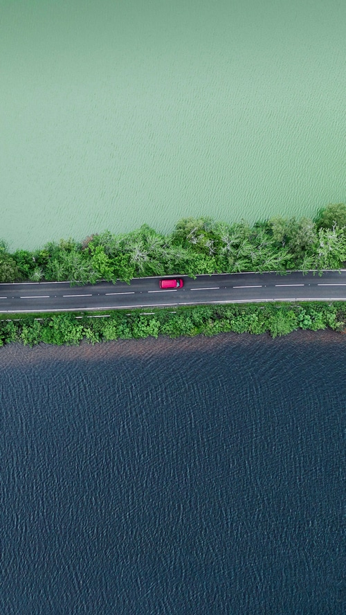 Aerial view of a red car on a road between two bodies of water