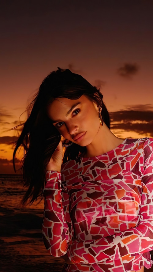 Emily Ratajkowski poses against a sunset beach backdrop