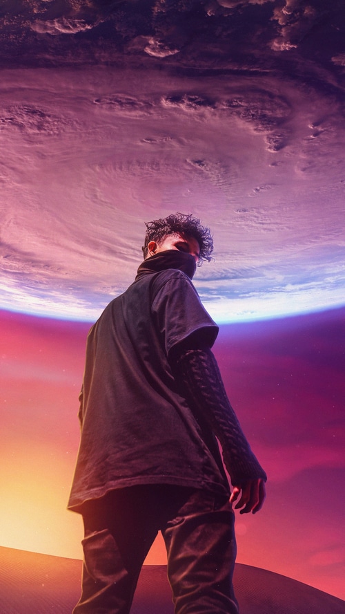 Man in black standing on desert planet with nebula sky