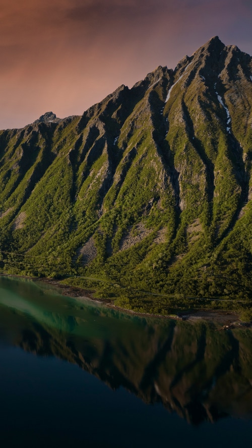 Green mountains reflected in a dark lake at sunset