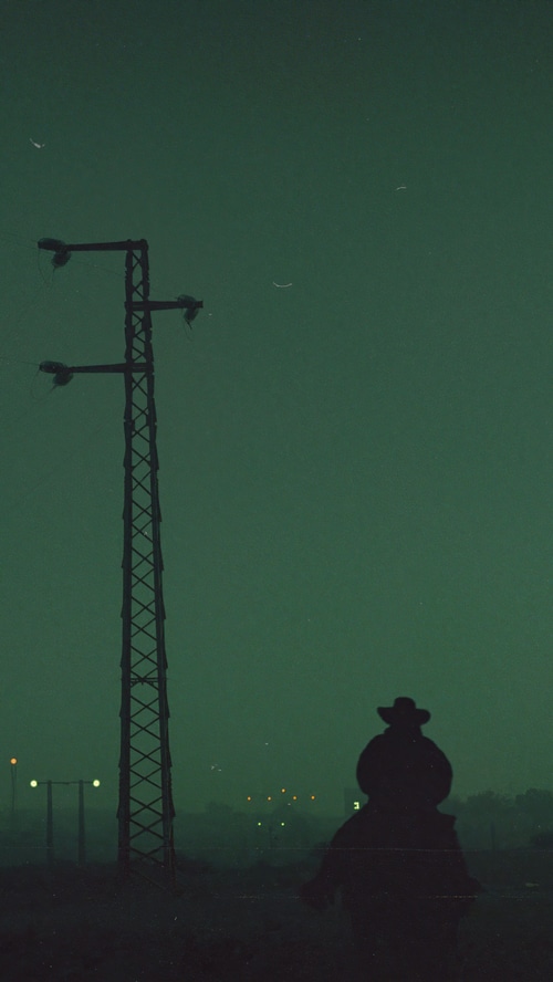 Silhouette of a figure with a cowboy hat against a dark sky