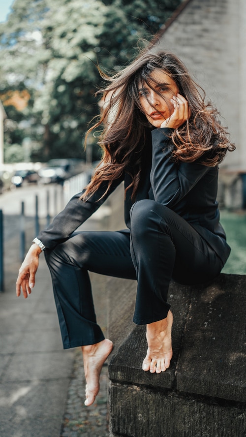 Woman in black suit sitting barefoot on stone wall