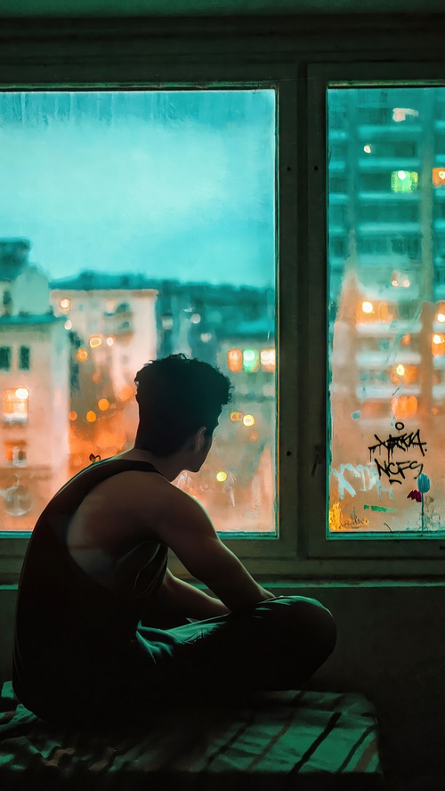 Man looking out a window at city lights
