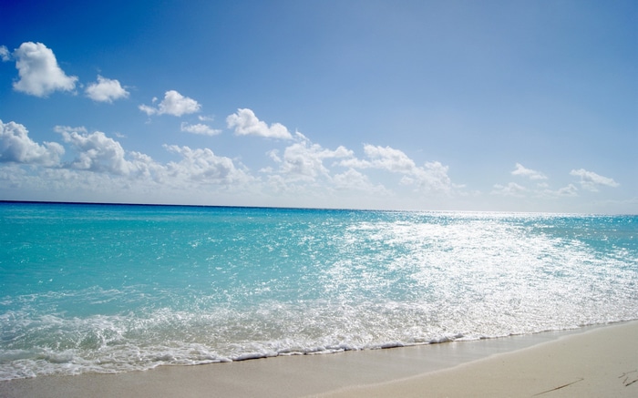 Turquoise ocean waves on a sandy beach under a blue sky