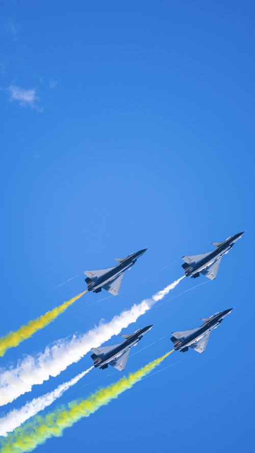 Four fighter jets flying in formation with colored smoke trails