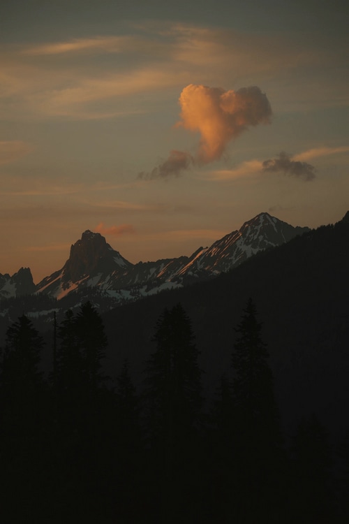 Heart-shaped cloud over snowy mountains at sunset